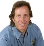 D'Arcy Swanson looks directly at the camera with a smile, shoulder length brown hair and a denim button down shirt.