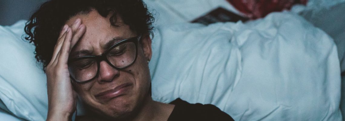 Latin American woman crying while sitting next to her bed