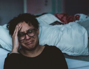 Latin American woman crying while sitting next to her bed