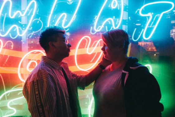 Couple looking at each other and touching in front of neon sign