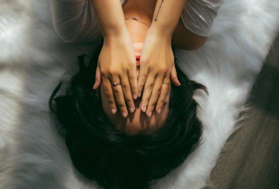 Woman laying on a bed covering her eyes with her hands