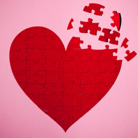 Red heart puzzle with the pieces coming together over a pink background